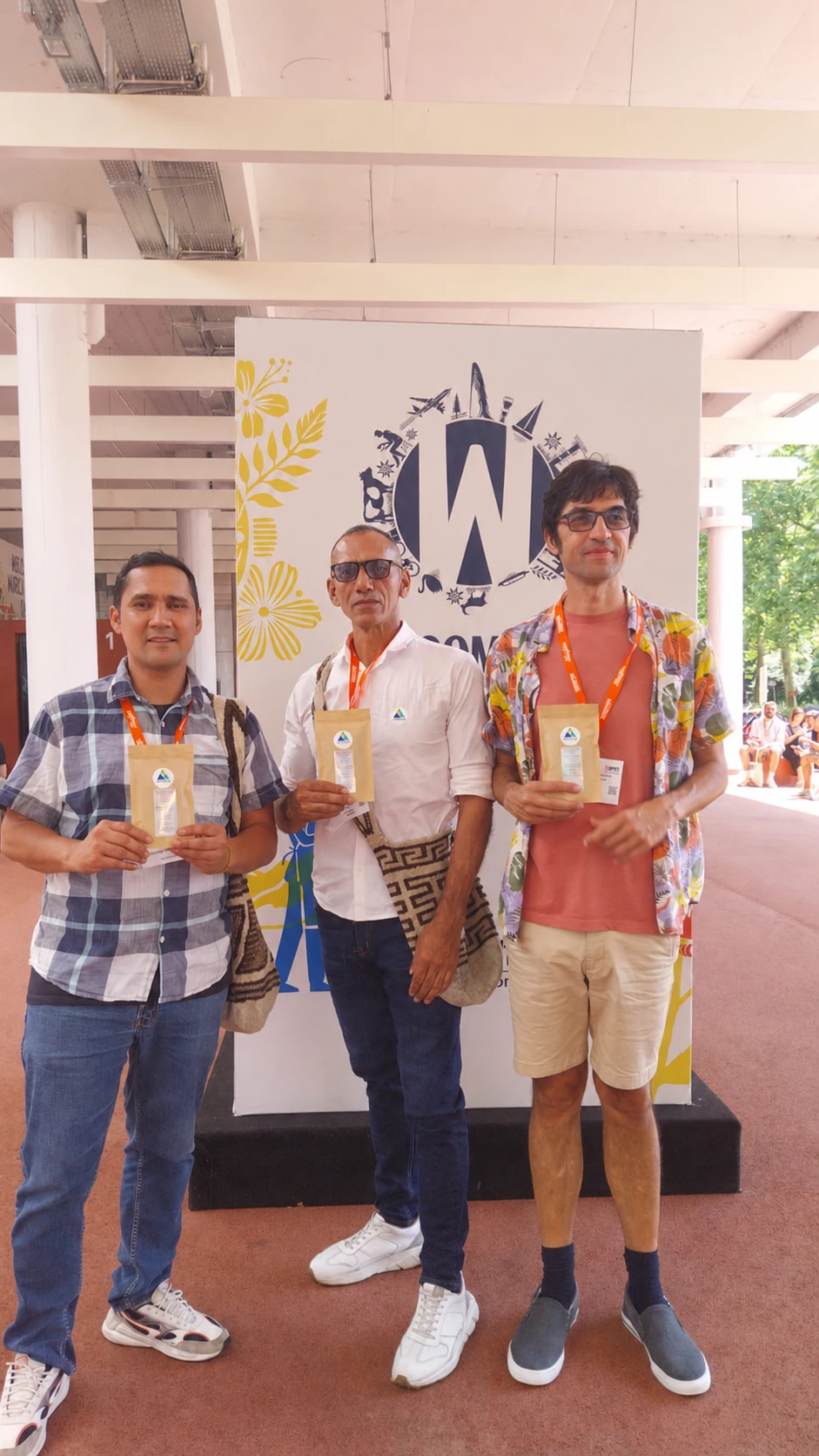 Tres participantes con café colombiano frente al emblema de World of Coffee
